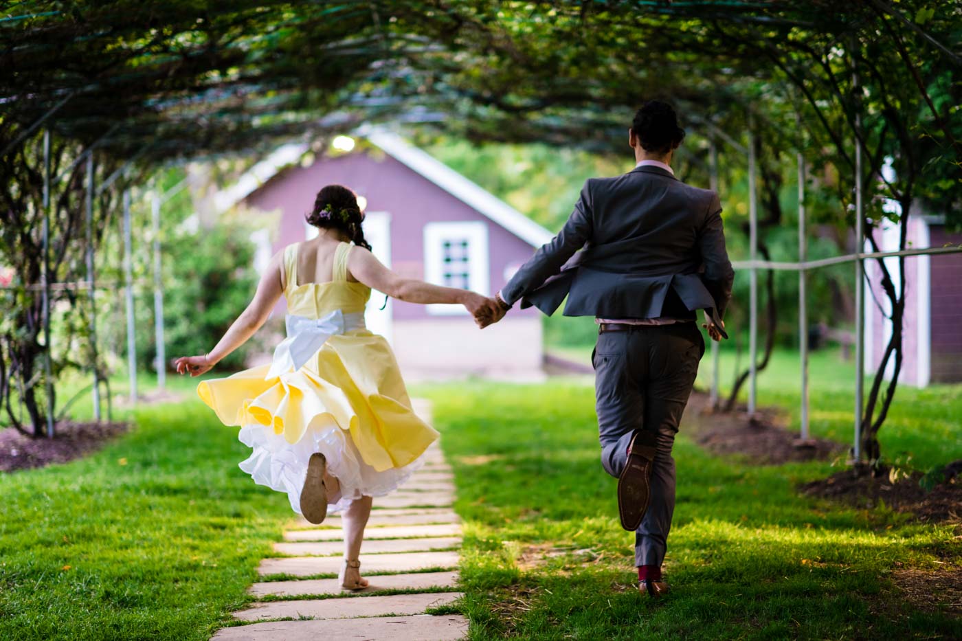 newlyweds-running-hand-in-hand-dow-the-garden-path