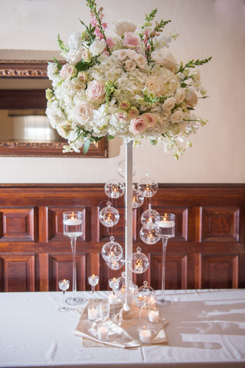 white floral arrangement in a high vase with hanging glass globes for votive candles